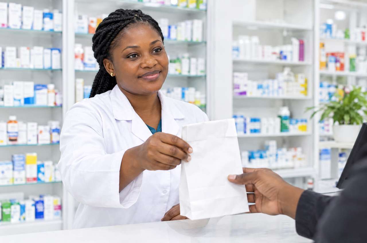 Une pharmacienne tend un sachet au comptoir.